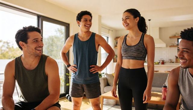 Friends exercising together in sunlit open-plan living room sharing laughter and casual stretching