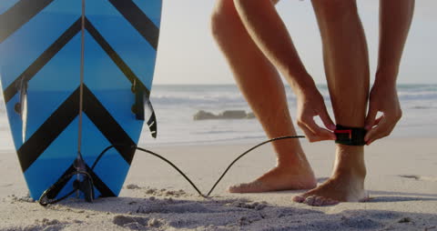 Surfer Preparing by Fastening Leash on Ocean Beach