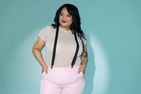 Curvy model posing in pastel high-waist pants with black suspenders on teal backdrop