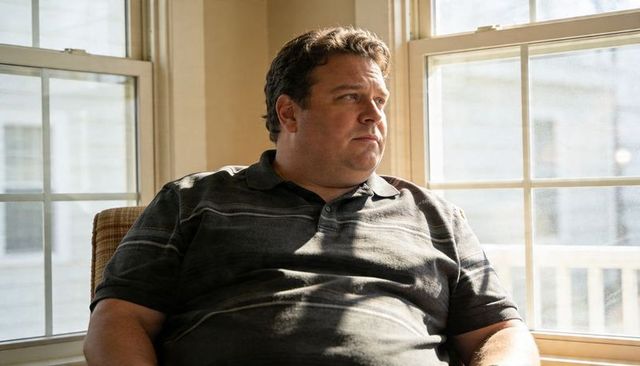 Middle-aged man gazing out window in sunlit room sitting in cushioned chair, contemplative mood