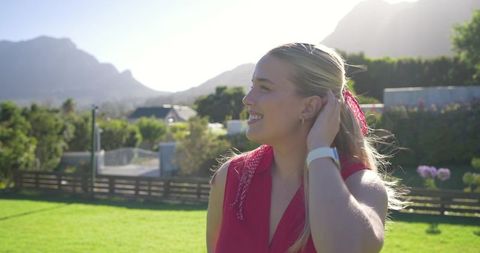 Young woman enjoying sunlit suburban garden breeze wearing red top scarf and white smartwatch