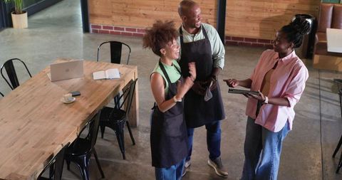 African american cafe team discussing orders with tablet in minimalist coffeehouse