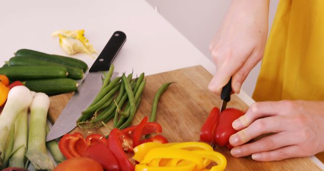 Person chopping colorful vegetables on a wooden cutting board. Bell peppers, green beans, zucchini, and leeks are visible. Useful for content related to healthy eating, cooking tutorials, culinary classes, nutrition, fresh produce, and home cooking tips.