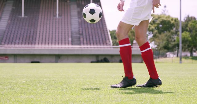 Soccer player in red and white uniform practicing on an outdoor field. Ideal for use in sports-related content, training programs, athletic events promotion, and physical fitness campaigns.
