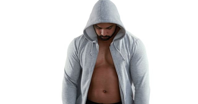 A young Caucasian man stands with his head bowed, wearing a hooded sweatshirt unzipped to reveal his bare chest, with copy space. His introspective pose suggests a moment of contemplation or determination.