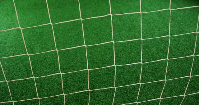 Shows close-up of soccer goal net with green synthetic turf in background. Perfect for use in sports-related content, advertisements for sports equipment, or backgrounds for recreational activities.