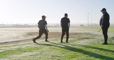 Coach leading baseball training at sunrise, athletes practicing on dew-covered infield