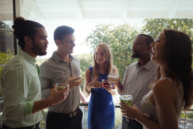 Group of friends enjoying cocktails while socializing at an outdoor gathering. Ideal for use in advertisements for social events, summer parties, or lifestyle blogs focusing on friendship and leisure activities.