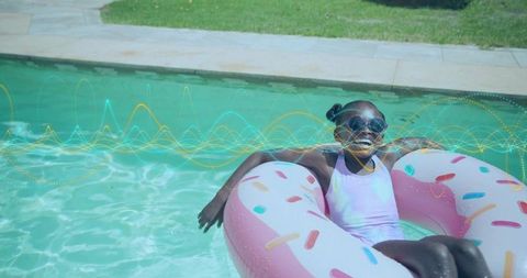 Smiling girl floating on donut pool float in backyard pool enjoying sunny summer