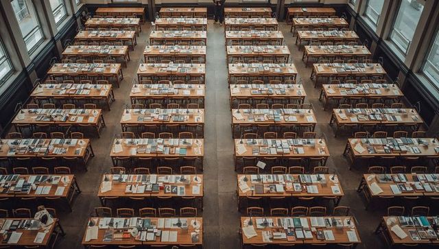 Grand historic reading hall showing long wooden study tables, rows of vintage lamps, overhead view