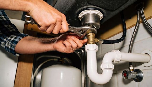 Handyman tightening p-trap under kitchen sink with adjustable wrench