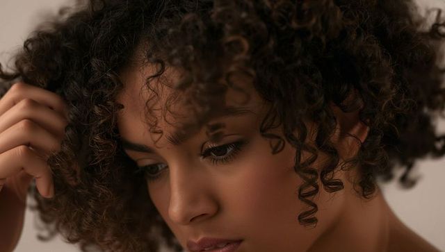 Touching curly hair, woman tilting head downward with soft makeup and mascara lashes