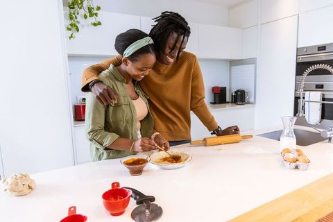 African american couple baking pie together in modern kitchen, smiling and embracing