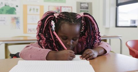 Focused Girl with Pink Braids Writing in Classroom