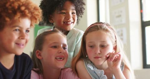 Diverse primary school children collaborating around table in bright classroom, smiling
