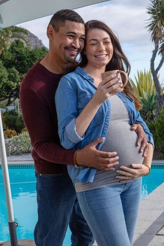 Expectant couple embracing by poolside on a serene day