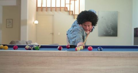 Leaning and aiming pool cue on blue-felt billiard table in modern cozy living room showing focus