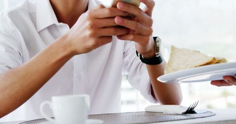 Young man browsing smartphone during meal at cafe
