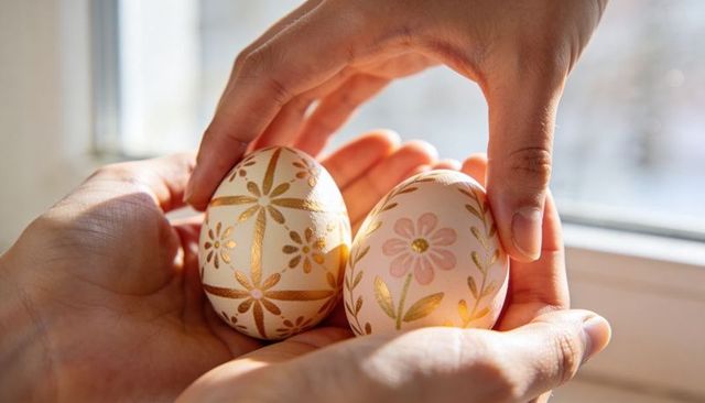 Hands cradling hand-decorated gold floral eggs near sunlit window for easter decor