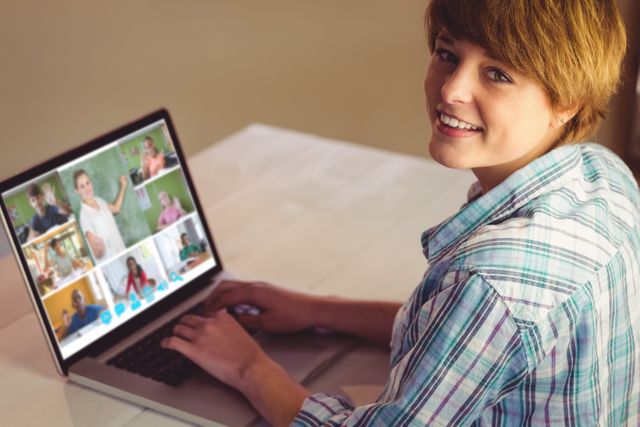 Young woman is smiling while engaging in an online meeting on her laptop from a home office. This image can be used to illustrate themes of remote work, virtual meetings, and modern technology for business or educational purposes. Ideal for articles about telecommuting, digital communication tools, or home office setups.