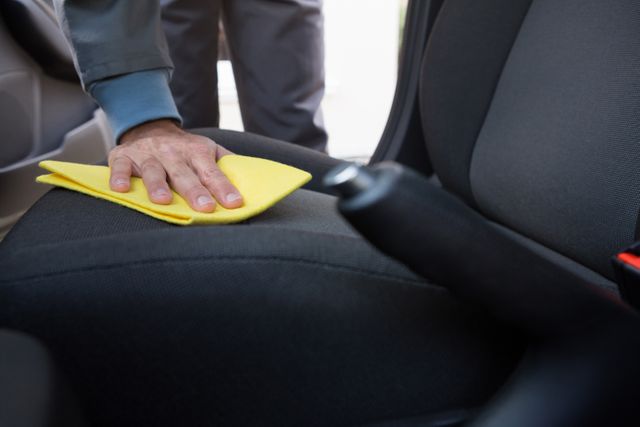 This image shows a worker cleaning a car seat with a yellow cloth, focusing on maintaining the cleanliness and hygiene of the vehicle's interior. Ideal for use in automotive maintenance advertisements, car detailing service promotions, and articles on vehicle care and hygiene.