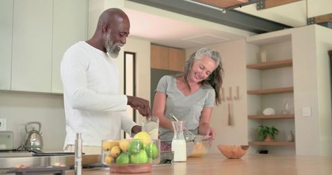 Senior black man and white woman cooking at modern kitchen island, pouring and stirring