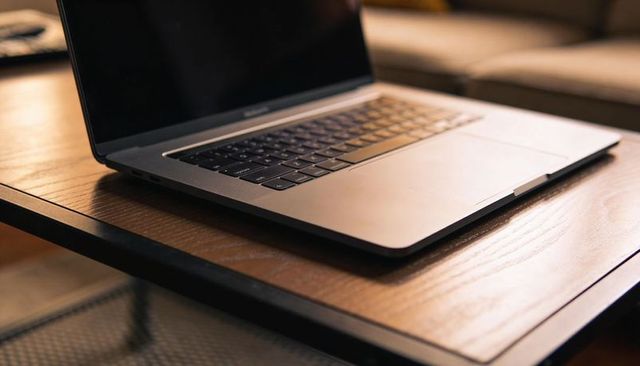 Minimalist metallic laptop resting on wooden table with oversized trackpad and keyboard