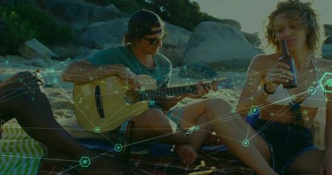 Young friends playing guitar and relaxing on beach with glowing network overlay