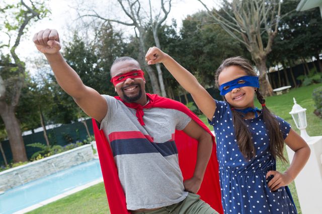 Father and daughter dressed as superheroes, enjoying playful bonding time in backyard. Perfect for themes of family fun, imagination, parenting, and childhood joy. Ideal for advertisements, blogs, and articles about family activities, fatherhood, and creative play.