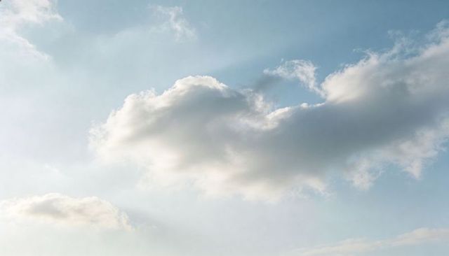 Soft cumulus cloud drifting across blue sky with gentle light and minimalist composition
