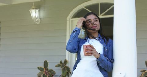 Enjoying morning coffee on porch while leaning against column wearing denim jacket