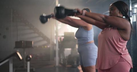 Diverse mid-adult women performing kettlebell swings together in gym for strength