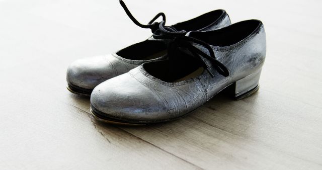 A pair of metallic tap shoes with black laces rests on a wooden floor, evoking the world of dance and performance. Tap shoes like these are essential for dancers to create rhythmic sounds and showcase their tap dancing skills.