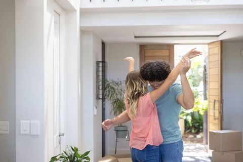 Young couple dancing and embracing in sunny entryway amid moving boxes, new home joy