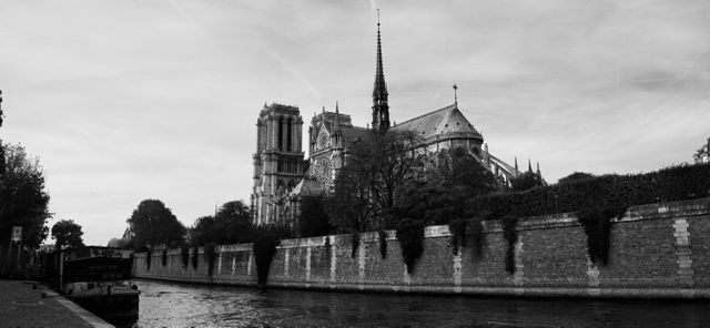 Black and white view of Notre Dame Cathedral taken from River Seine. The cathedral shows gothic architecture and historic significance. Suitable for travel websites, architectural studies, historical references, and European tourist guides.