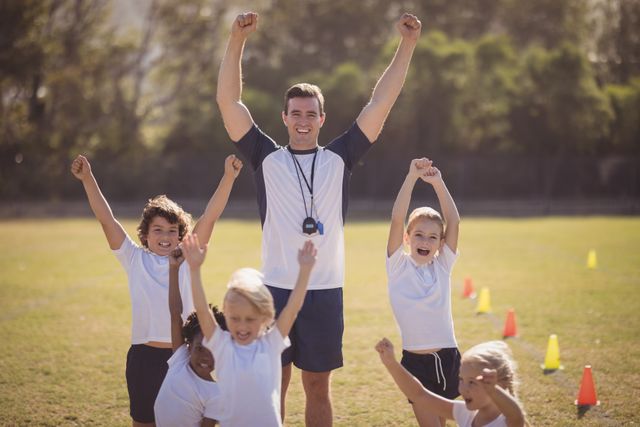 Coach and schoolchildren are seen celebrating a victory outdoors in a park. The group is cheering with arms raised, showcasing teamwork and joy. This image is ideal for promoting physical education, teamwork, and outdoor activities for children. It can be used in educational materials, sports event promotions, and advertisements for youth fitness programs.