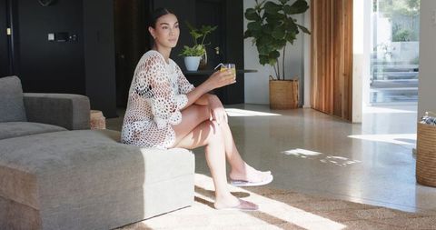 Sunlit living room with woman in crochet cover-up sipping citrus drink on terrazzo floor