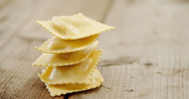 Four pieces of ravioli stacked neatly on a rustic wooden surface. Appears fresh and homemade, showcasing traditional Italian cuisine. Perfect for use in culinary blogs, recipe websites, and gourmet food promotions.