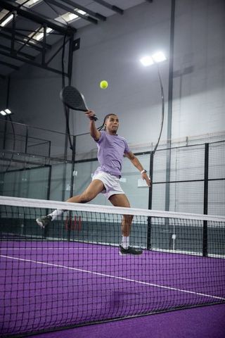 Male athlete jumping and swinging paddle for smash on purple padel court indoor arena