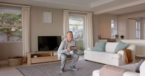 Senior man exercising with dumbbells in living room upholding fitness