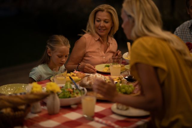Happy multi-generation Caucasian family eating a meal at home, standing and serving food to his family, mother, grandmother and granddaughter enjoying time together at the table