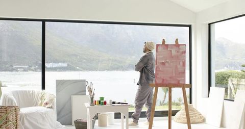 Indian artist standing contemplating canvas in lakeside studio with panoramic window view