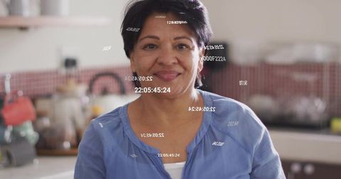 Senior woman smiling in kitchen wearing blue blouse with digital timestamp overlay