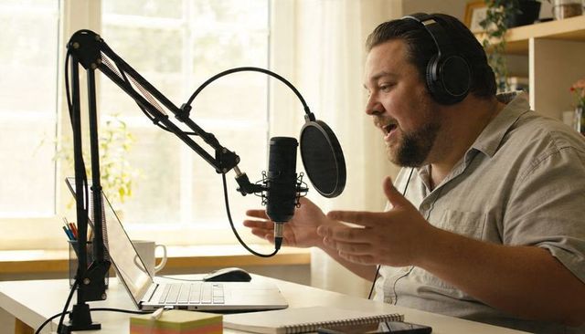 Podcast host recording and speaking from home studio with condenser microphone and laptop