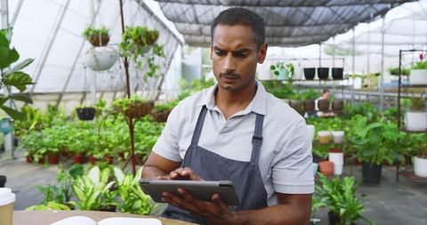 Botanist Using Tablet in Greenhouse Surrounded by Lush Plants