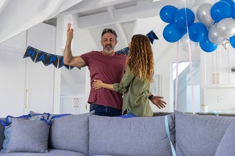 Middle-aged couple celebrating birthday in bright loft-style living room with blue balloons