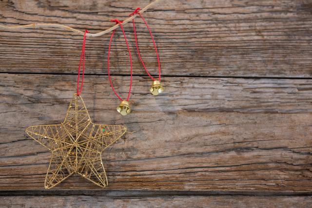 Christmas star and bell ornaments hanging on rustic wooden wall with red strings. Ideal for holiday greeting cards, festive invitations, seasonal blog posts, and Christmas-themed advertisements.
