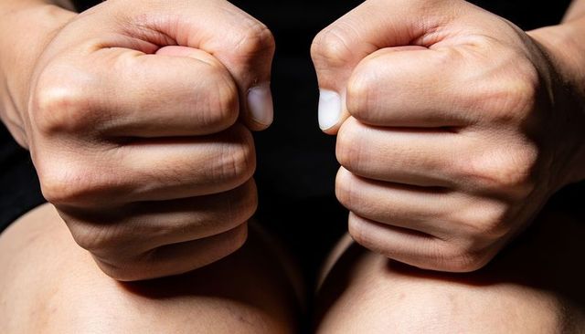 Clenching fists above bare knees showing knuckles, tense grip and skin texture closeup
