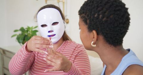 African american friends doing at-home skincare routine with led facial mask and serum