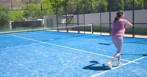 Woman swinging forehand on blue padel court during sunny outdoor sport and fitness play